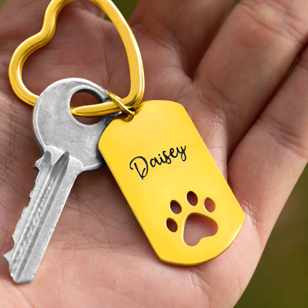 A hand is holding a Custom gold Paw dog tag keyring with text engraving